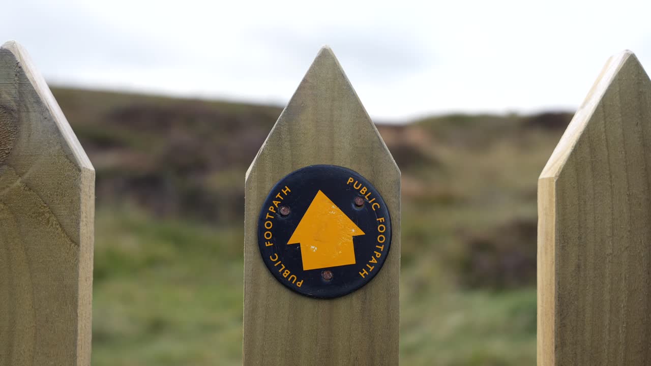 Public footpath sign on a wooden fence along British countryside hiking trails