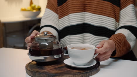 Woman-pouring-cup-of-tea-from-kettle-on-kitchen-counter