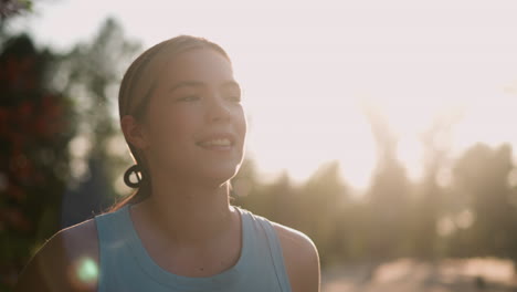 close-up of young lady smiling with sun glowing around her face, creating a warm, radiant backlit effect, she appears serene and joyful, hair tied back, with blurred trees in background