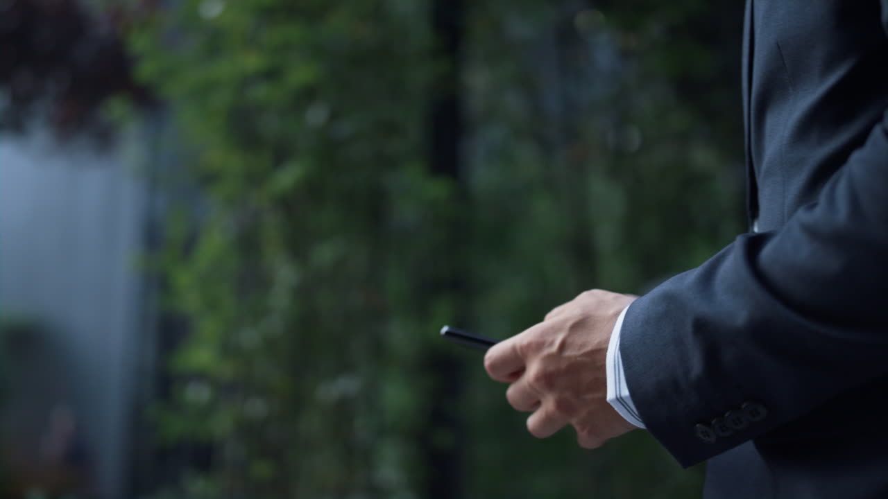 자신감 있는 사업가의 손으로 문자 메시지를 보내고 다운타운 지구를 가까이 걸어다니고 있습니다.