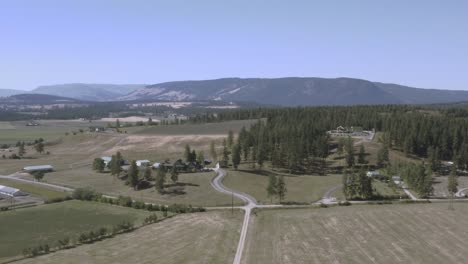 aerial panout fly over cattle farms rolling hills within a mountain valley township with luxury estates around ranches curvy roads on a hot clear summer day with moder barns tall lush pine trees 2-2