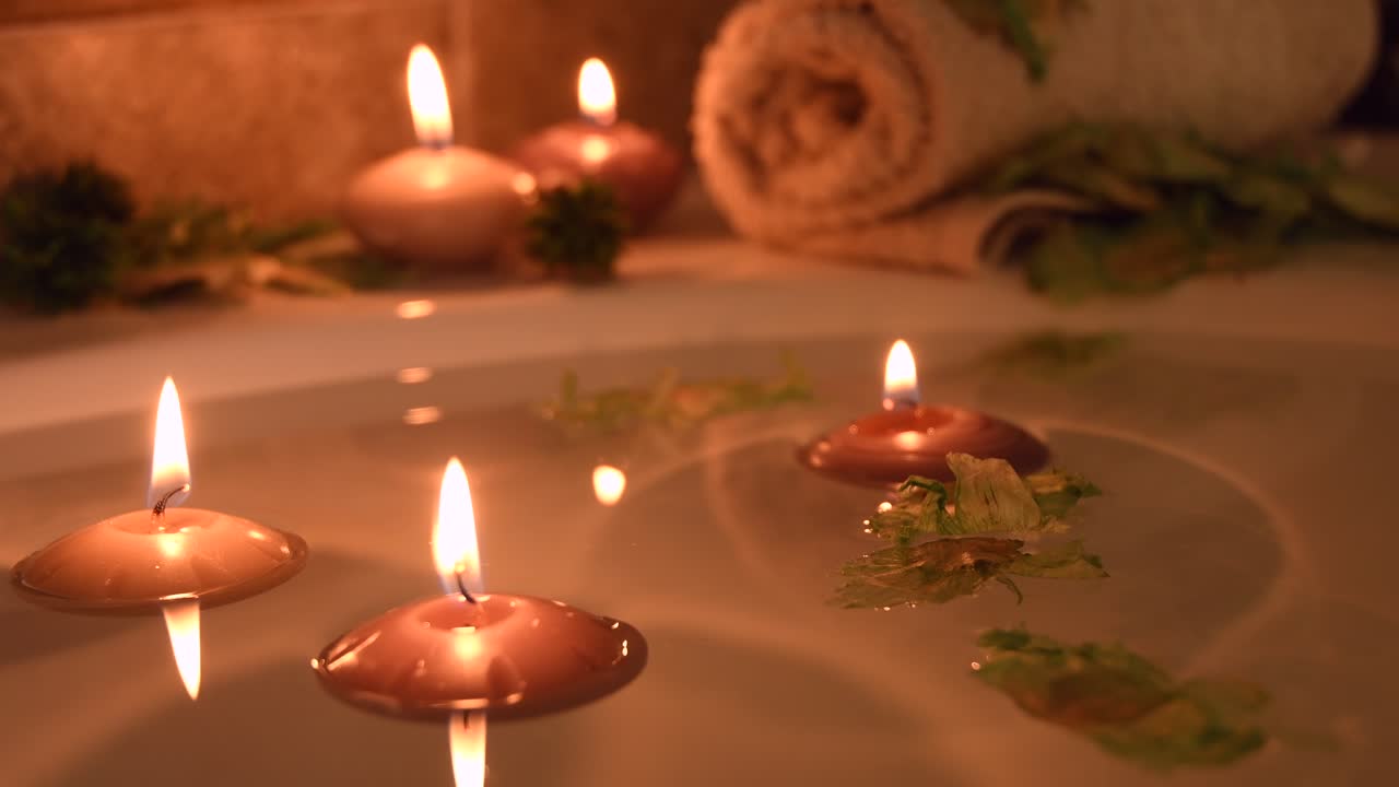 목욕물에 촛불이 떠 있는 편안한 스파 배경, 일부 녹색 꽃잎, 물 표면 근처의 수건