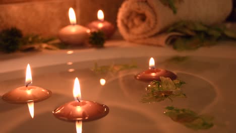 relaxing spa background with candles floating in the bath water, some green petals and a towel near the water surface