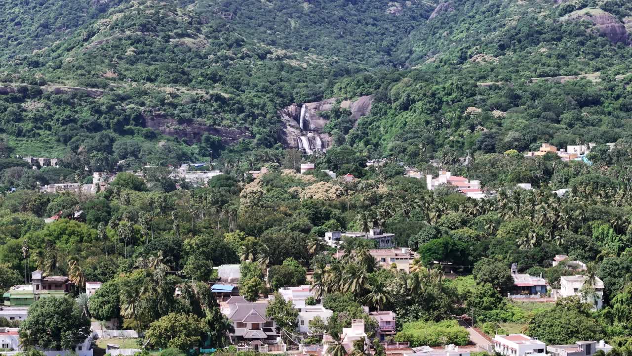 Stunning aerial view of Courtallam Main Falls in Tamil Nadu in the South Indian hills, flowing into a town surrounded by a lush green forest. Ideal for travel, nature, and tourism-related content