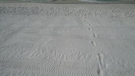 aerial view of foot prints on the white sands of florida to the clear emerald waters of the gulf of mexico on a bright sunny summer day