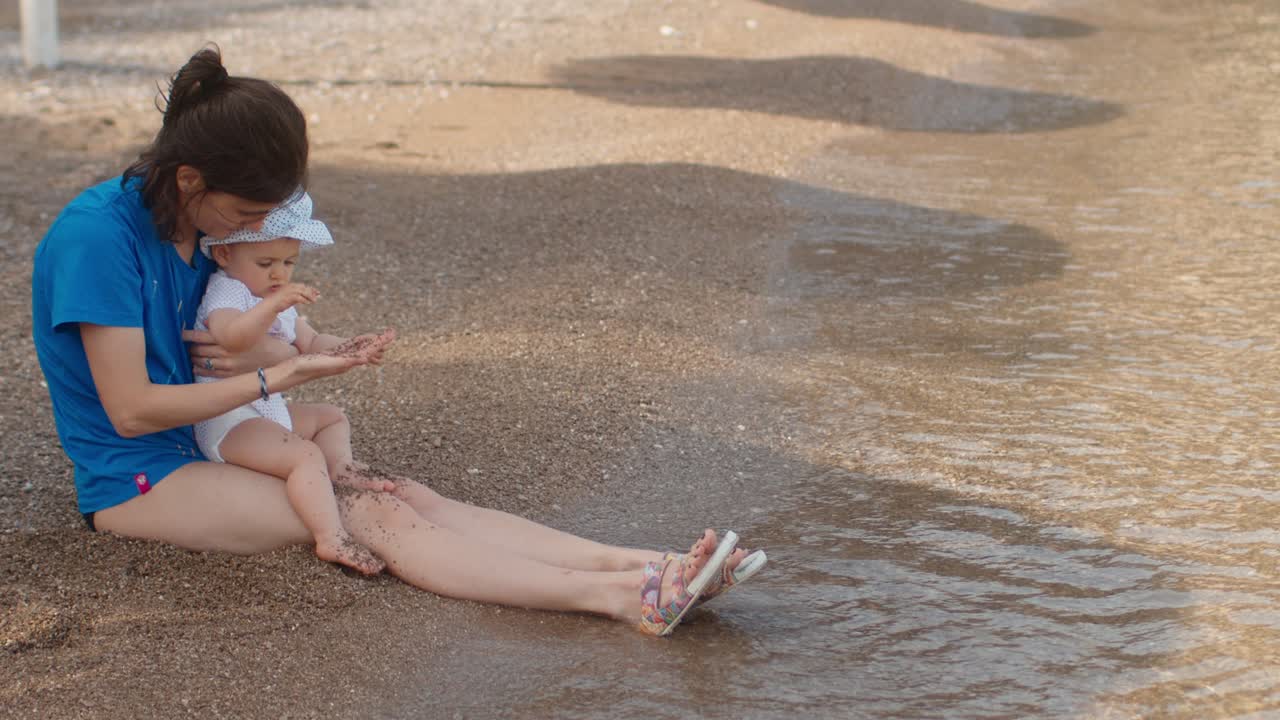 어머니와 딸은 해변에 앉아 모래로 놀고 있습니다.