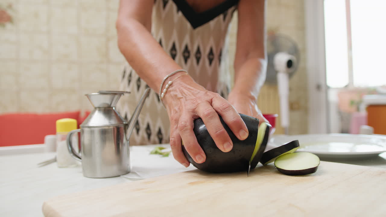 Una donna taglia melanzane fatte in casa su un tagliere per preparare la parmigiana siciliana