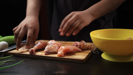 transferir trozos de pollo a un tazón amarillo desde una tabla de cortar de madera con las manos