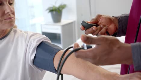 african american male doctor checking blood pressure of caucasian female patient at hospital