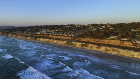 aerial view rising up from waves, in front of a luxury neighborhood, golden hour in san diego, california, usa