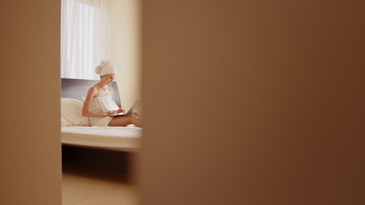 머리에 수건을 고 침대에서 노트북을 쓰고 있는 여자