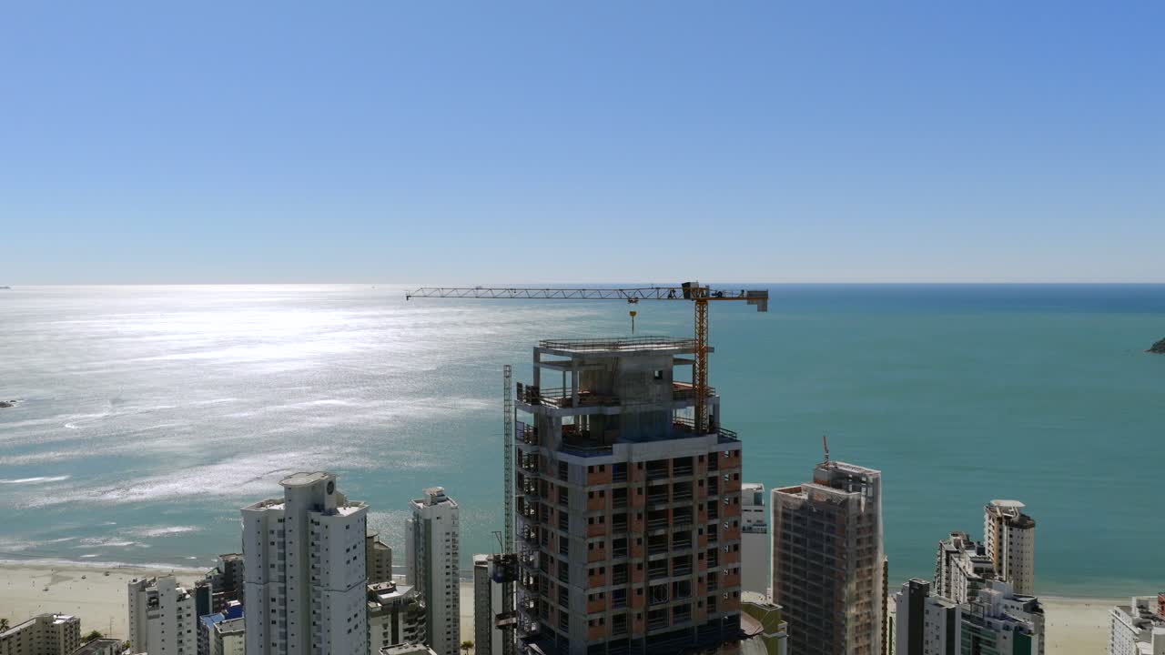 Construction crane building skyscraper on the coast of Balneario Camboriu, State of Santa Catarina, Brazil, with a view of the Atlantic Ocean, on a sunny day