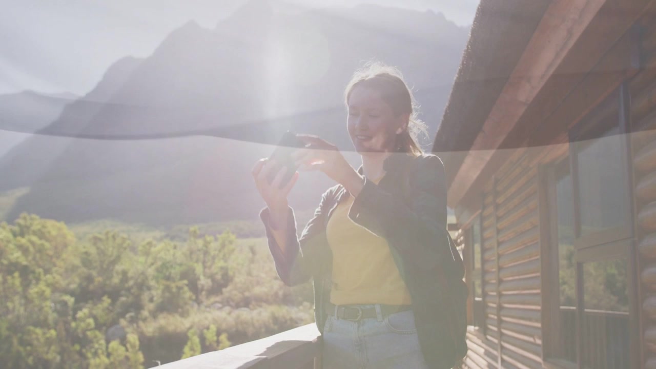 Woman raising smartphone to sunlit mountains, framing then lowering phone and reviewing travel shot