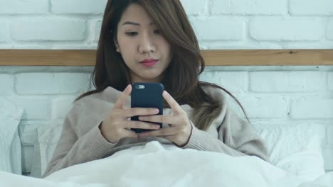 happy asian women are using smart phone on the bed in morning. asian woman in bed checking social apps with smartphone. smiling woman surfing net with cellphone at home. mobile addict concept.