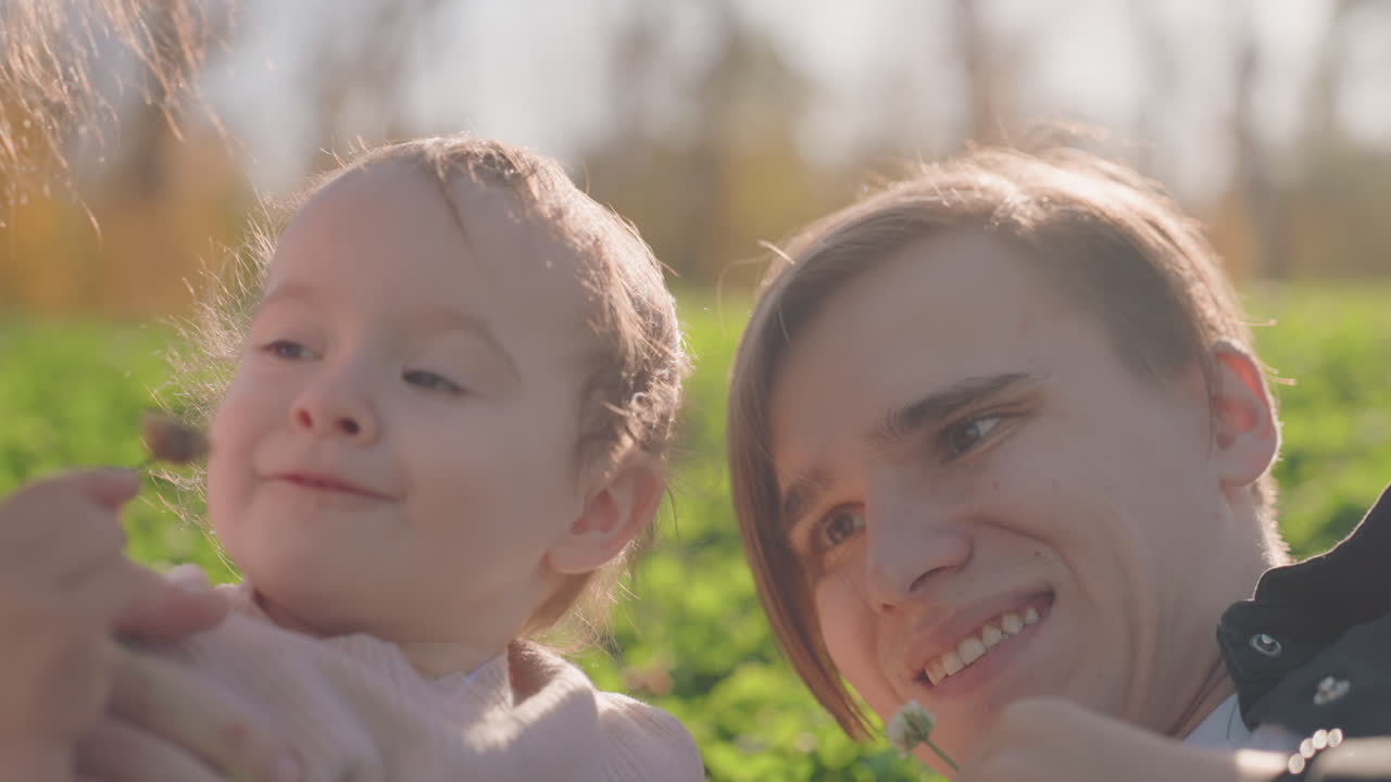 Padre e bambino in un campo soleggiato, interazione giocosa a un picnic in famiglia con genitori che condividono risate e solletico delicato, sullo sfondo un prato verde, un momento spontaneo di connessione gioiosa e rilassata.