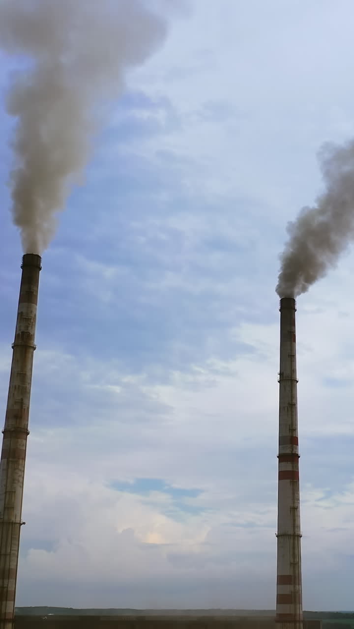 Enterprise chimneys tubing against the sky background release black smoke. Dangerous smoke against blue sky. Factory pollutes the environment. Vertical video