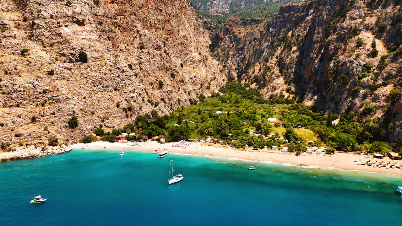 Approaching amazing idyllic beach hidden among the huge rocks. Few boats stand on the anchor near the shore. Turkey