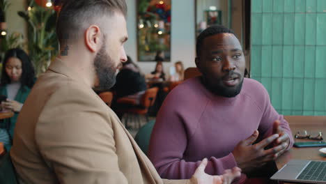 multiethnic men discussing project on laptop on business lunch in cafe