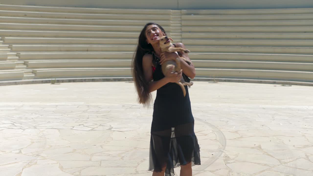 Attractive Woman in Black Dress Holding Her Dog Puppy Pet in Center of Amphiteathre on Sunny Summer Day, Full Frame