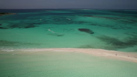 Crystal-clear-turquoise-waters-and-white-sand-beach-with-kite-surfers,-aerial-view