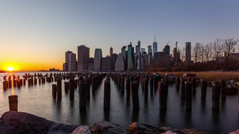 golden hour time lapse beyond manhattan skyline seen from old pier brooklyn park in nyc, united states