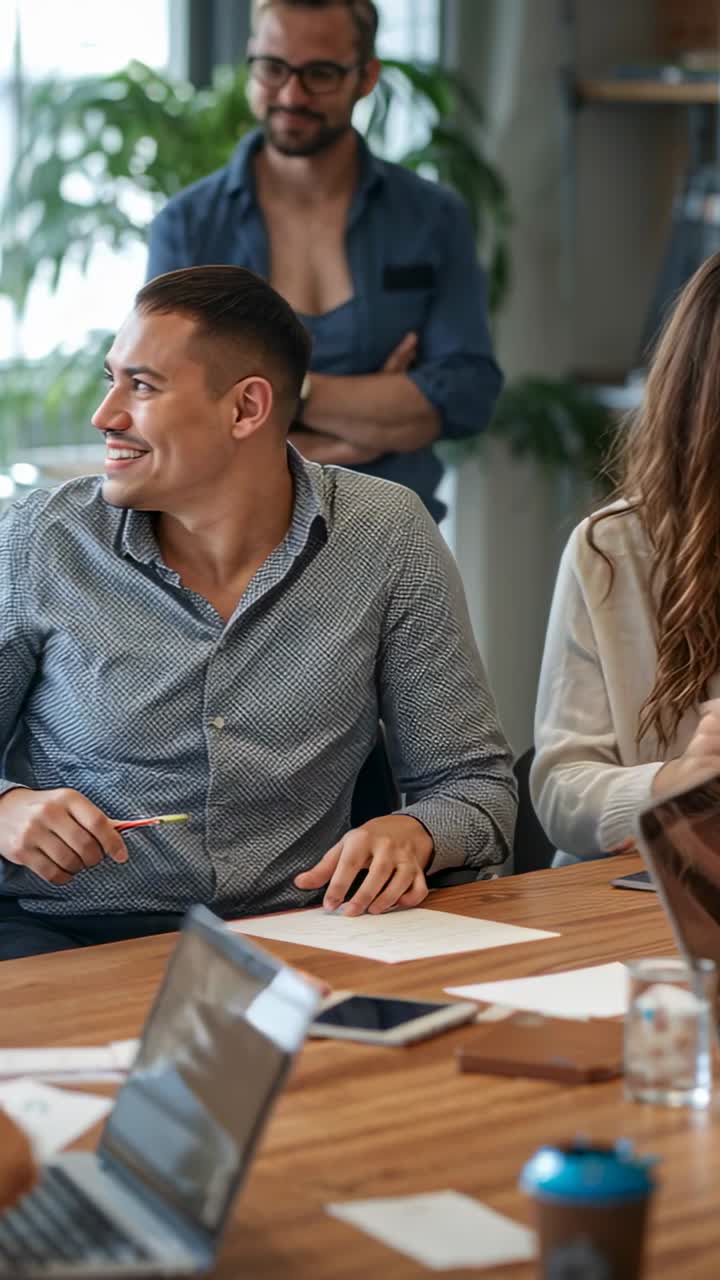 Vídeo vertical: Homem sorrindo com camisa estampada escrevendo com lápis depois de um colega de trabalho apontar em uma reunião
