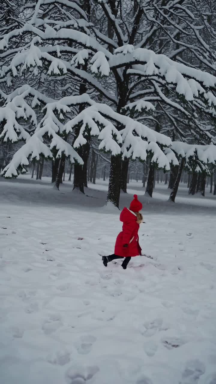 A child in a red coat runs joyfully through a snowy forest. Captured from a low angle, the video