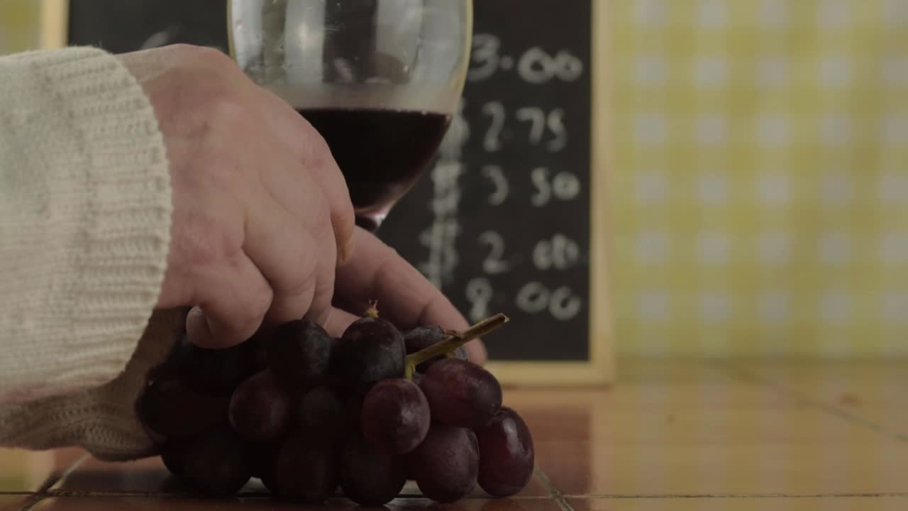 Hands holding glass of red wine eating grapes in cafe