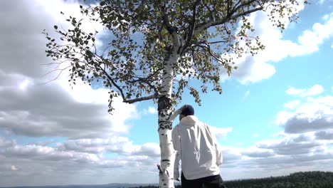 man looking up at a birch tree in a scenic landscape