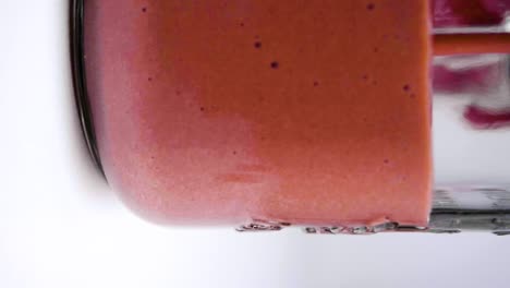 Vertical-slow-motion-shot-of-vegan-chocolate-protein-shake-being-poured-into-a-glass-against-a-white-background