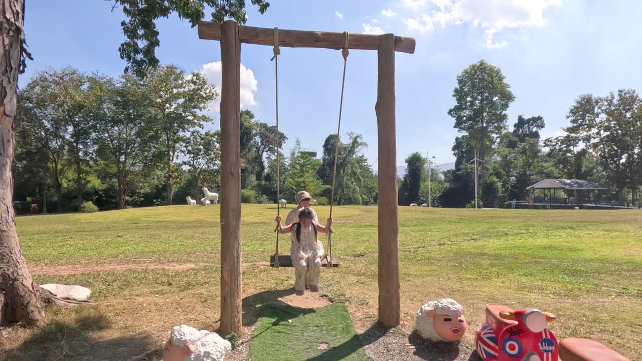 İki genç Taylandlı kız, güneşli bir parkta ahşap bir salıncakta keyifle oynuyor.
