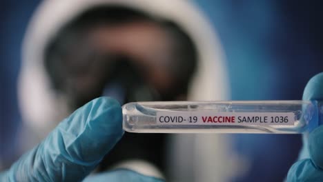primer plano de las manos con guantes de látex azules que sostienen el tubo de ensayo de la vacuna covid-19