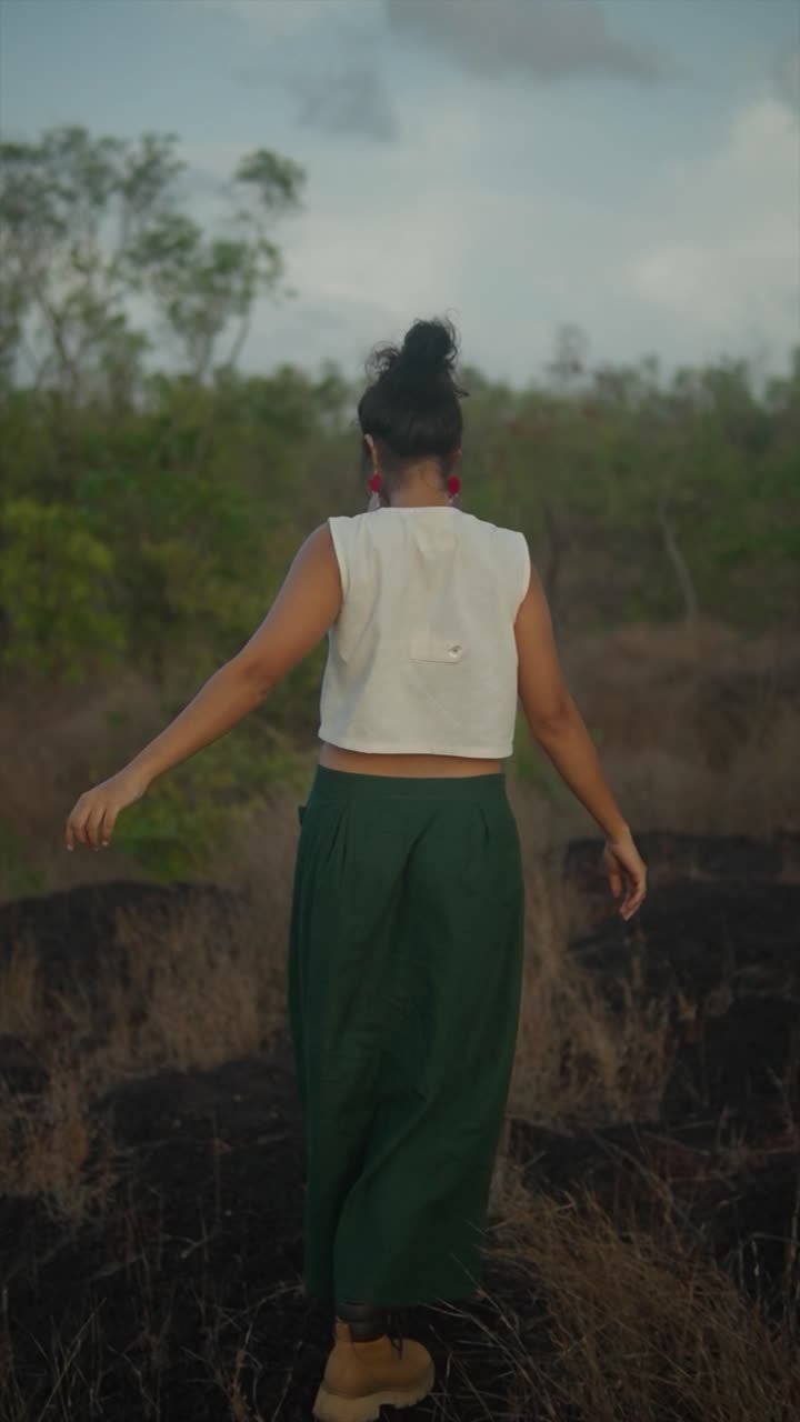 Indian woman in green pants and a crop top walks across a charred, dry forest area. India