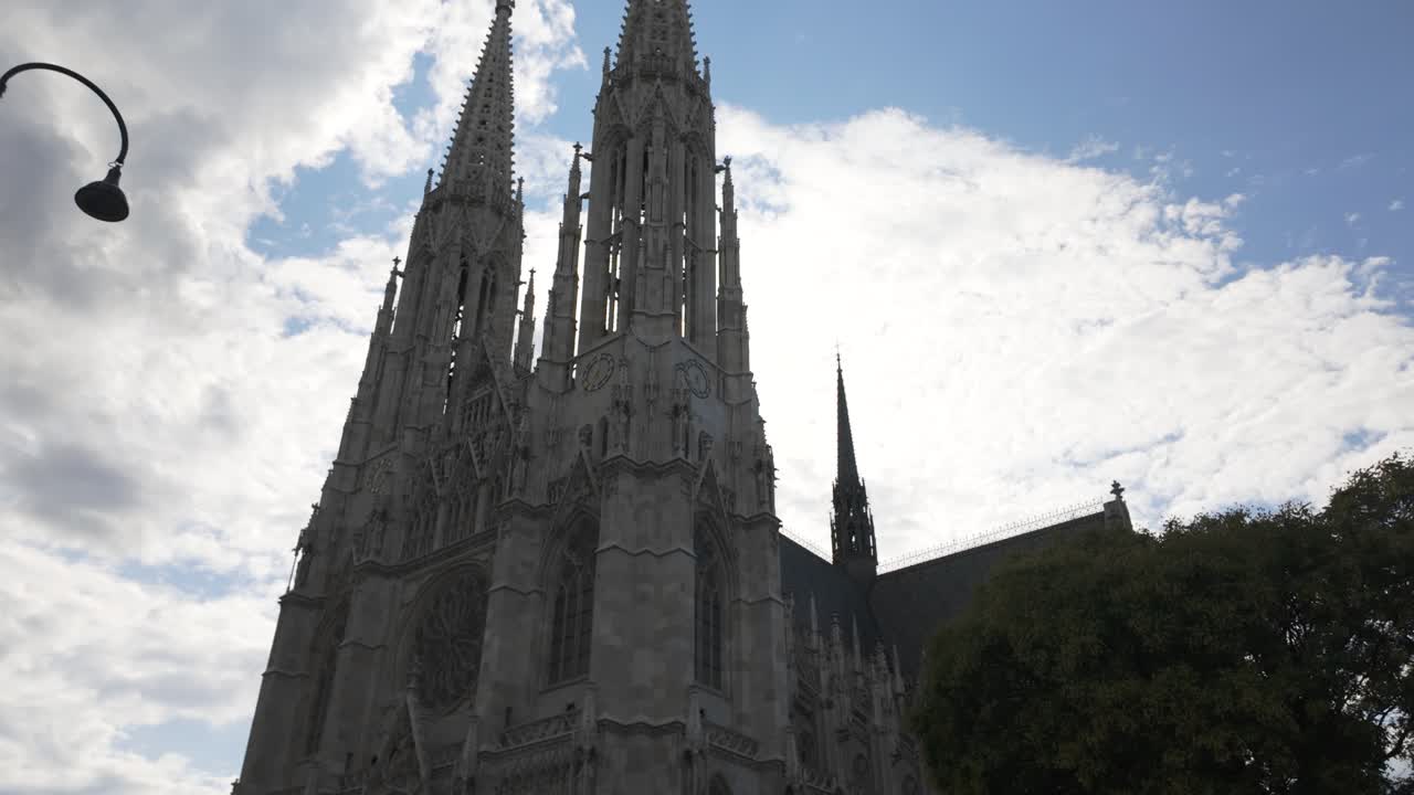 Exterior view of the Votive Church (Votivkirche) in Vienna, Austria, showcasing its Gothic architecture with intricate details and towering spires under a partly cloudy sky