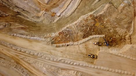 drone view of trucks and a bulldozer quarrying in a rock quarry - zoom out