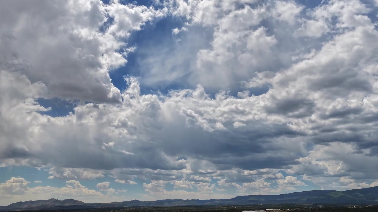 4K aerial timelapse capturing turbulent summer monsoon season clouds against a vibrant blue sky. Deep shadows sweep over the vast, brush-covered high desert and distant mountain ridges.