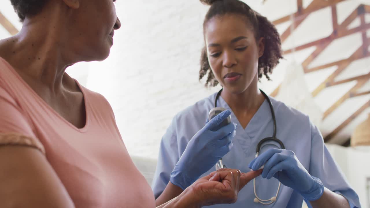 African american female doctor checking sugar levels of senior woman with glucometer at home