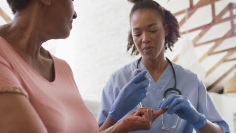 african american female doctor checking sugar levels of senior woman with glucometer at home