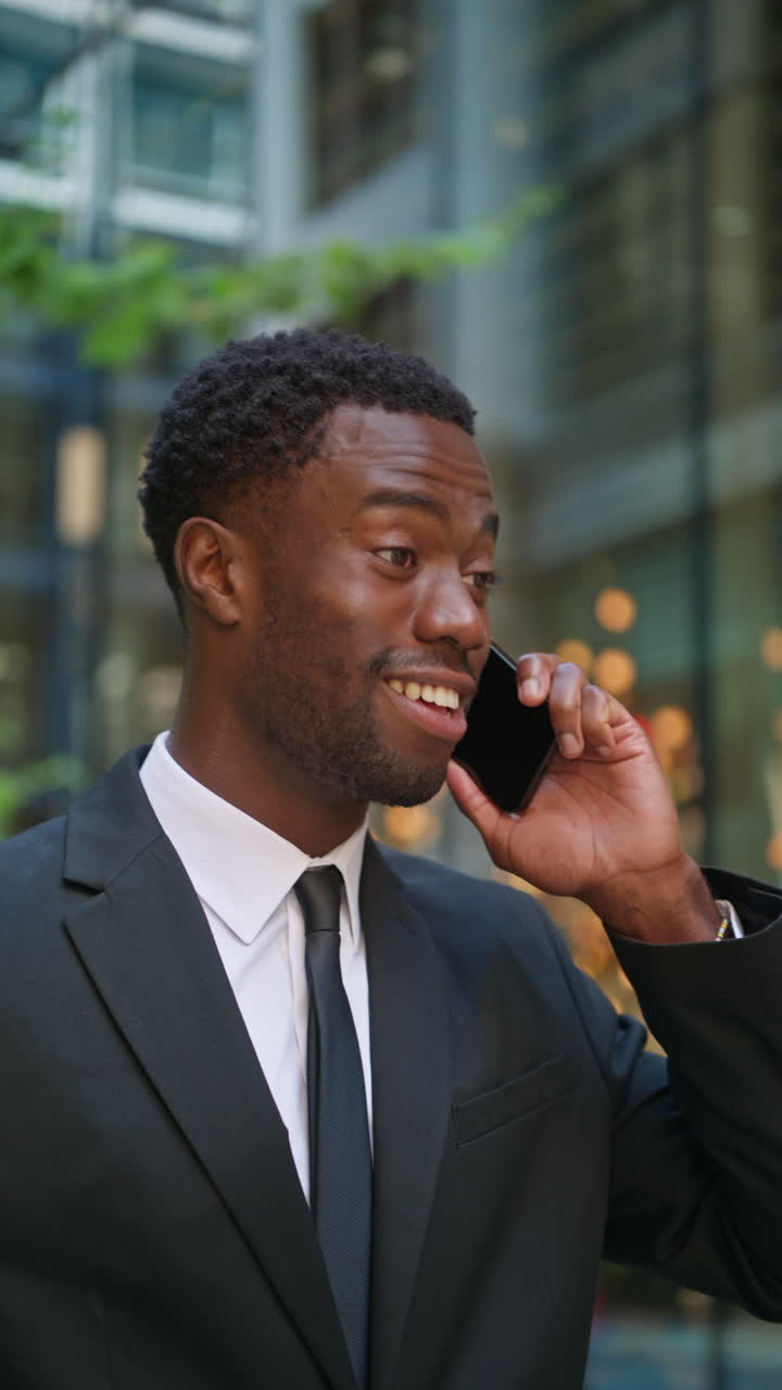 Vertical Video Shot Of Smiling Young Businessman Wearing Suit Talking On Mobile Phone Standing Outside Offices In The Financial District Of The City Of London UK Shot In Real Time 2