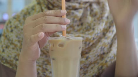 close-up of a person holding and drinking iced coffee