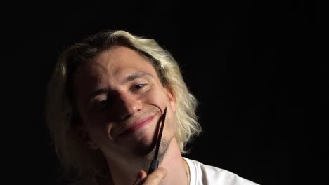 mad young blond long haired man playing with the knife around his face