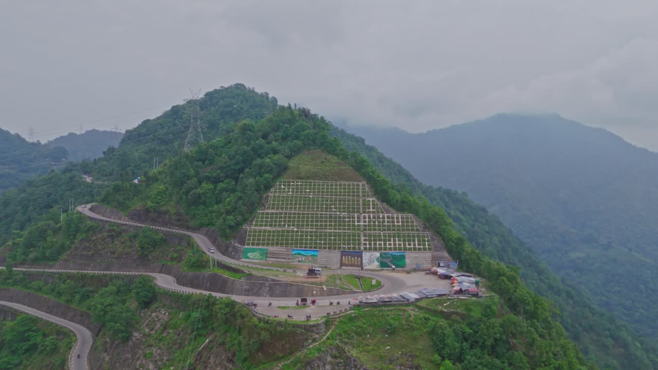 A serpentine road curves gracefully through vibrant green mountains, offering a breathtaking view of natural beauty and human engineering in harmony, captured from a high-altitude aerial perspective.