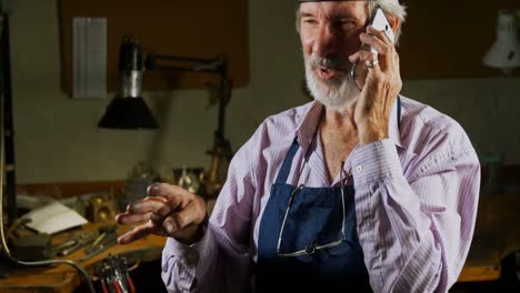 Goldsmith-talking-on-mobile-phone-in-work-shop-4k