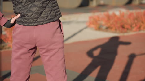 back view of student workout participant swaying waist sideways on sunny outdoor court with autumn shrubs behind, long shadows of figure stretching across red gym mats, focus on form and movement