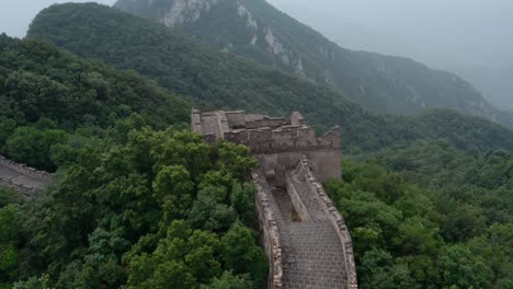 volar sobre la torre vigía deteriorada de la gran muralla china en la cima de la cordillera verde en un día nublado