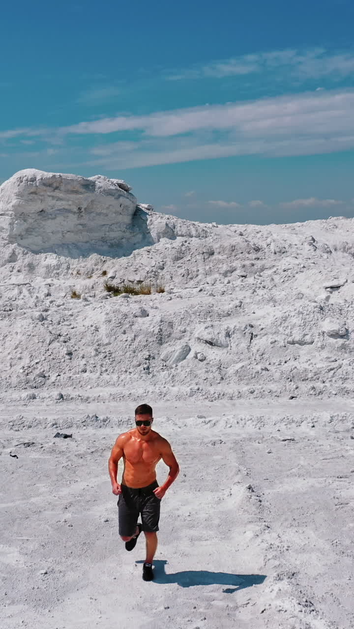 Muscular bodybuilder running on white rocky canyon. Shirtless man of fitness body doing his workout in the mountains in a warm sunny day. Camera moves back. Vertical video