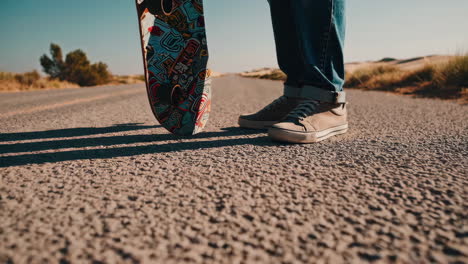 person holding a skateboard on an empty desert road
