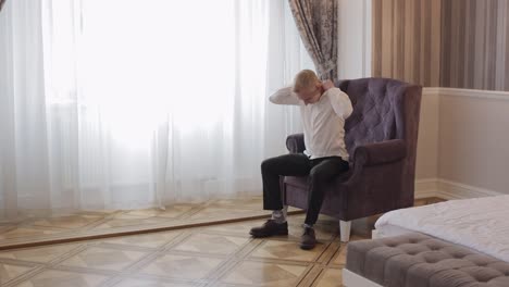 Stylish-businessman-groom-buttoning-white-shirt,-adjusting,-wearing,-putting-shoes-near-window