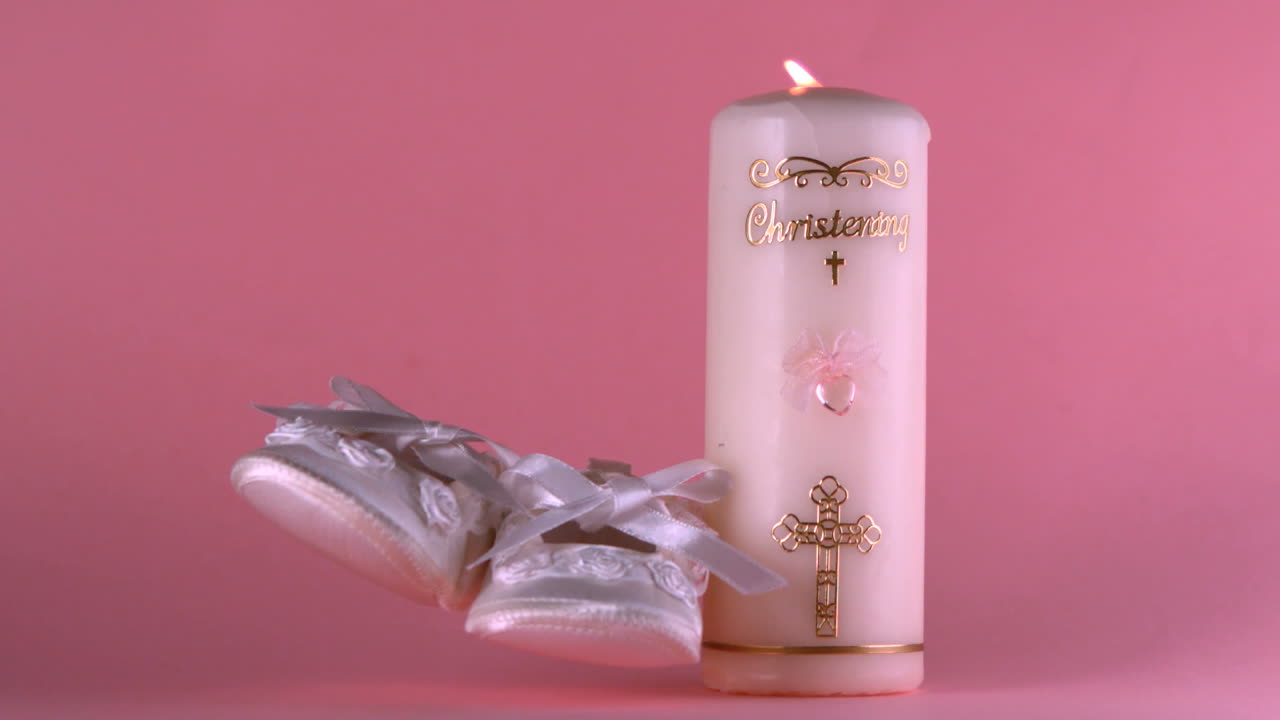 zapatos de bebé cayendo al lado de la vela de bautismo encendida