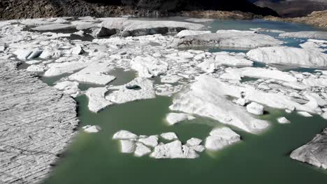 sobrevuelo aéreo sobre un lago glaciar lleno de icebergs derretidos en partes remotas de los alpes suizos en un día soleado con una sartén desde el hielo hasta los picos montañosos cubiertos de nubes